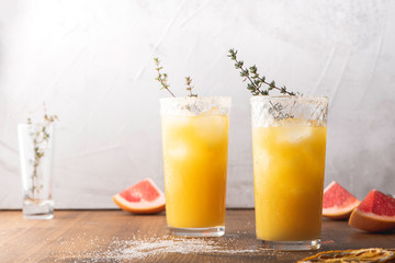 Citrus juice with ice in glass glasses and slices of fruits on a wooden table, light grey background, front view.
