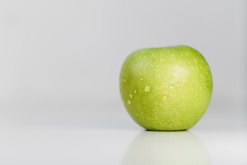 Fresh green apples with water droplets on a white glossy kitchen table. Tasty bright juicy fruits. Healthy eating. Isolated object.