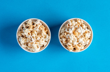 Two white bowls with popcron on a blue background, top view, flat lay. Free space for text. Background with popcorn.