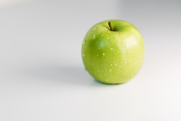 Fresh green apples with water droplets on a white glossy kitchen table. Tasty bright juicy fruits. Healthy eating. Isolated object.