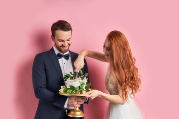 Bearded man in tuxedo and woman in white dress holding sweet cake, celebrate their wedding day together