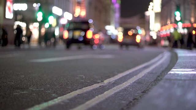 Closeup of road at famous London Piccadilly square with LED reflection cars driving by in blurry background. Night time city bokeh urban street scene in United Kingdom.