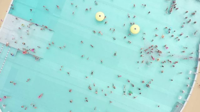 Aerial View Of Open-air City Pool In Warsaw. Poland. Crowds Of People Sunbathe And Swim In The Blue Clear Water In The Water Park. Sunny Day Aerial Crowded Waves Waterpark Pool Down Panorama.