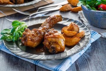 Chicken drumsticks in ginger beer sauce with potato wedges and salad on a plate