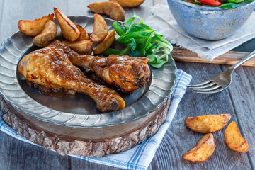 Chicken drumsticks in ginger beer sauce with potato wedges and salad on a plate