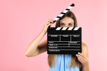 Young woman with black clapper board on pink background