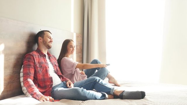 Beautiful charming girl spending time with handsome boyfriend watching TV, stretching hand trying to change TV program, free time concept