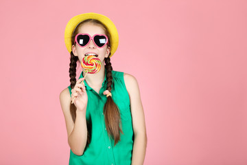 Beautiful young girl with sweet lollipop on pink background