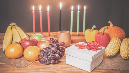 Kwanzaa holiday concept with decorate seven candles red, black and green, gift box, pumpkin,corn and fruit on wooden desk and background.