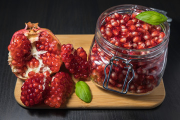 Delicious pomegranate seeds placed in glass jar with fresh organic pomegranates on rustic wooden background.Close up,Copy space