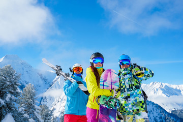 Two men and woman with snowboard and skis standing on snow resort against background of mountain...
