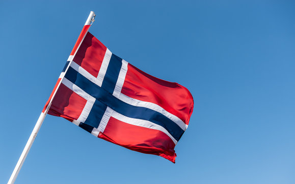 Flag of Norway. Norwegian flag on flagpole waving in the wind against blue sky. 