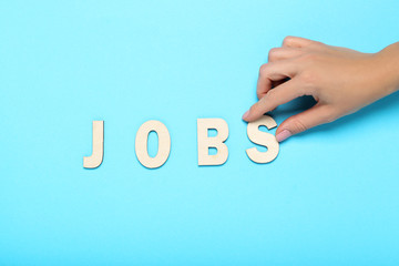 Word Jobs by wooden letters with female hand on blue background