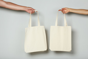 Female hands holding white cotton eco bags on grey background