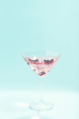 Cocktail in glass with eyelashes on blue background. Minimalism concept