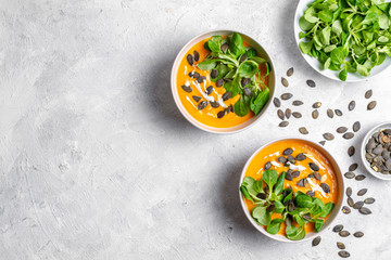 Two bowls of pumpkin soup with seeds and lettuce on light, white background. Copy space 