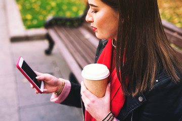 Woman sitting on a bench with beverage and phone.