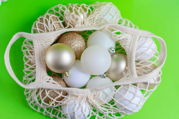 Christmas balls in eco friendly cotton bag on green background. White and golden balls for Christmas tree. 