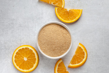 Orange peel powder in white bowl with oranges slices on light grey background