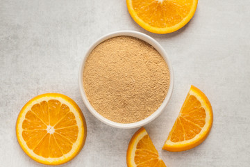Orange peel powder with oranges slices on light grey background