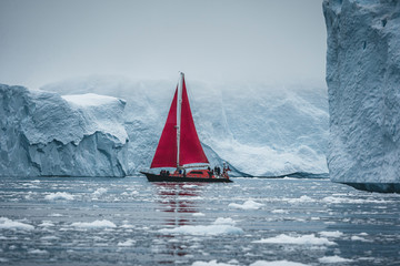 A small boat among icebergs. Sailboat cruising among floating icebergs in Disko Bay glacier during...