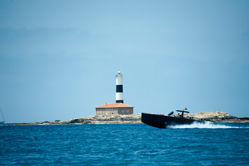 black boat sailing at high speed with the lighthouse of formentera in the background