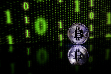 Bitcoin coin with reflection on a black background with a green binary code