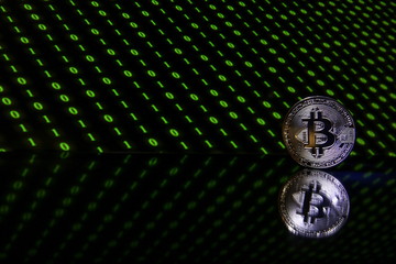 Bitcoin coin with reflection on a black background with a green binary code