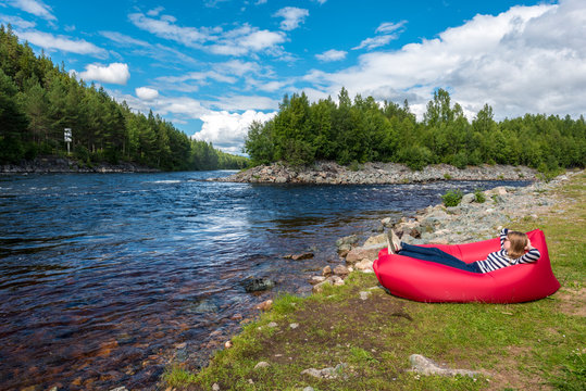 Young woman is relaxing in the red airlounger in the border of Fugga river in Hedmark county of Norway