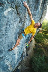 Young strong man climbing challenging route on a high vertical limestone cliff.