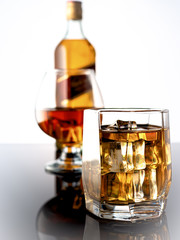 Glass of whiskey with ice on a dark background. In the background a glass with whiskey and a bottle of whiskey