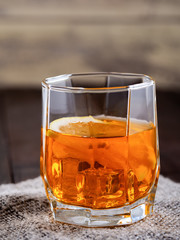 Glass of whiskey with ice on rustic background