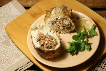 Baked fish luce stuffed  with buckwheat, lemon slice, parsley on  plate on rustic cover on wooden background