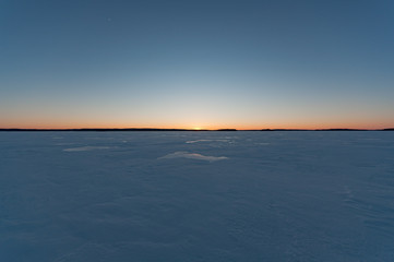 Sunset behind a vast field of ice of a frozen lake in winter in Finland