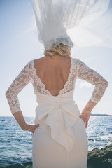 Beautiful bride in luxury wedding dress at the sea side. Wedding by the sea. Bride walking around the sea near the place of the wedding ceremony. Back view