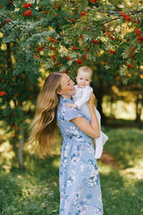 A young happy mother holds her baby son in her arms against the background of Rowan branches with berries, they are cheerful. Happy motherhood and childhood