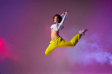Pleasant playful woman with long curly brunette hair, bright yellow pants, white pullover, wearing...