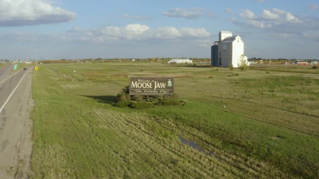 View of field and street sign in Moose Jaw, Saskatchewan, Canada. 4k drone footage, pano from left to right above road and prairies. House in the background.