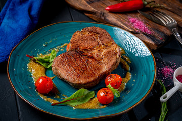 Large grilled beef steak on a plate with cherry tomatoes and mustard in plate on wooden dark background