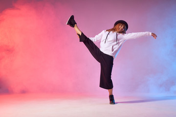Flexible young dancer doing split leap in the air, raising leg intensively up, bending back, stretching hand sideways, standing on one leg, enjoying dancing, looking away, athletic modern style dance