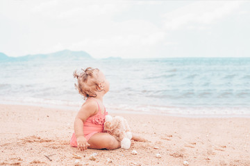 pensive little girl hugging teddy bear and looking away while sitting on seashore.