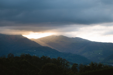 Fototapeta na wymiar Epic sunset light entering through the clouds between two big mountains in Basque Country