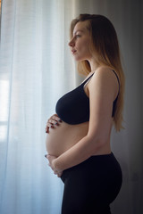 Portrait of young pregnant attractive woman, standing by the window
