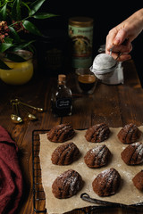 Homemade bakery chocolate madeleine cookies on cooling rack with ingredients and utensils on rustic wooden background