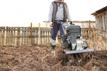 cultivating soil with gasoline cultivator. the farmer works the land before planting. man digs the ground with a diesel cultivator. farmer cultivates the land by a moto cultivator