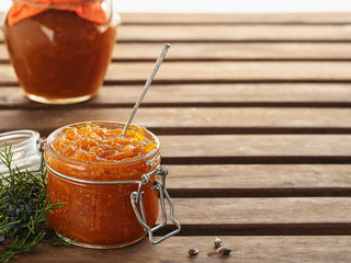 Tasty, homemade orange jam in a glass jar on a brown wooden background. Nearby is a branch of coniferous tree. Dessert spoon in a jar of jam. Healthy citrus dessert. Close-up, copy space for text.