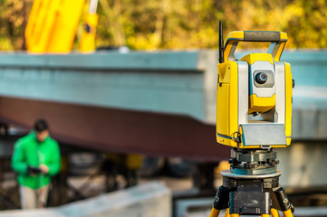 Surveyor engineer with equipment (theodolite or total positioning station) on the construction site of the road, building or bridge with construction machinery background