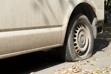 Old white flat van truck on the road. A flat tire in the autumn with leaves, near an old rusty.
