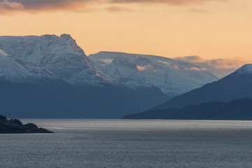 Mountains by a fjord with some snow and sunset colors in the sky in northern Norway