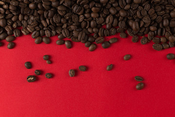 Coffee beans are scattered on a red paper background close-up, commercial copy space.